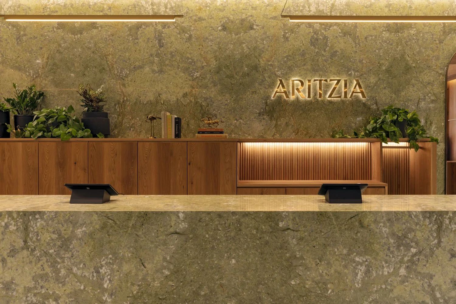 Stone checkout counter with timber cabinetry, plants, and illuminated Aritzia signage at Aritzia, Salt Lake City