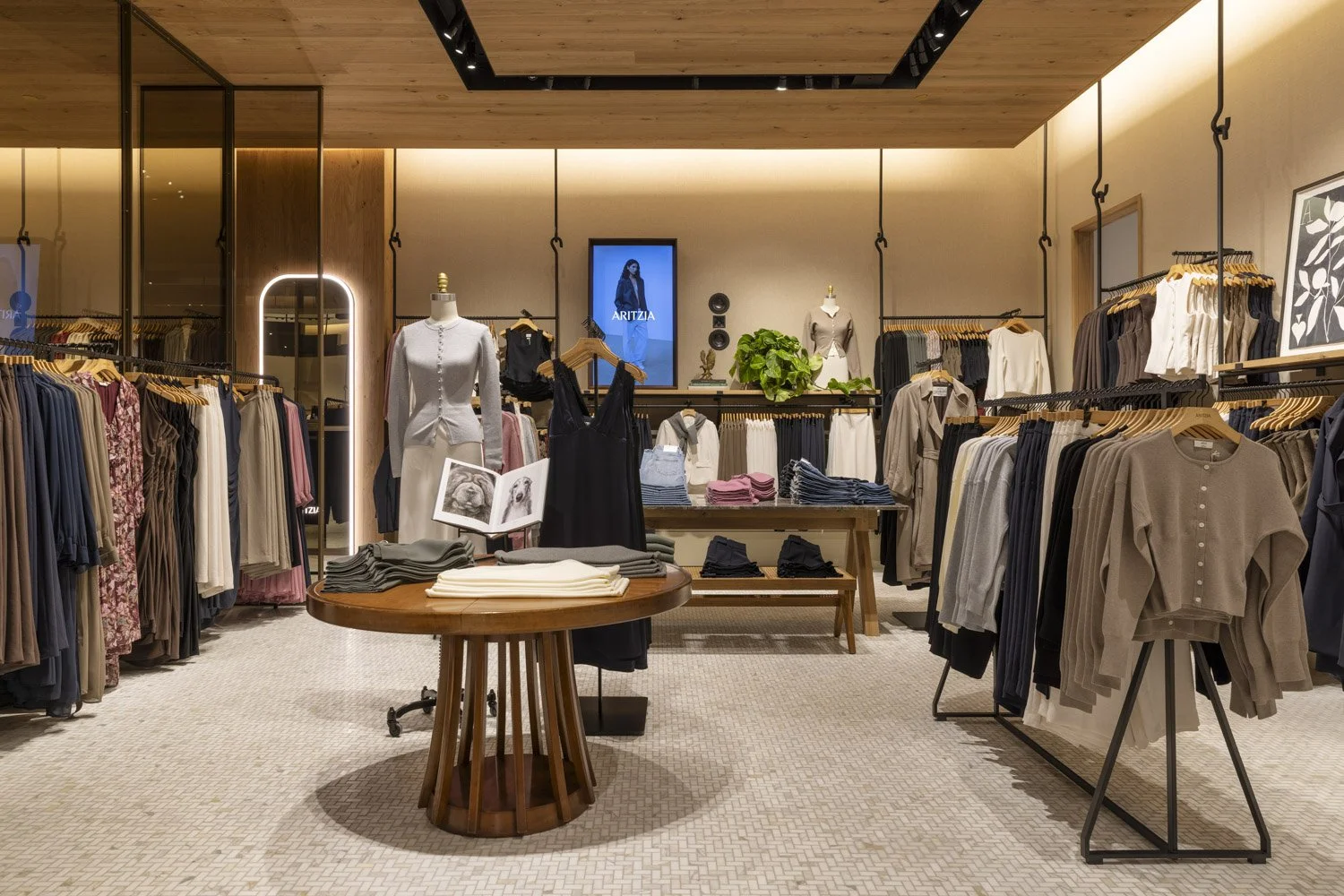 Clothing displays and timber tables beneath a wood ceiling with suspended garment rails at Aritzia, Salt Lake City