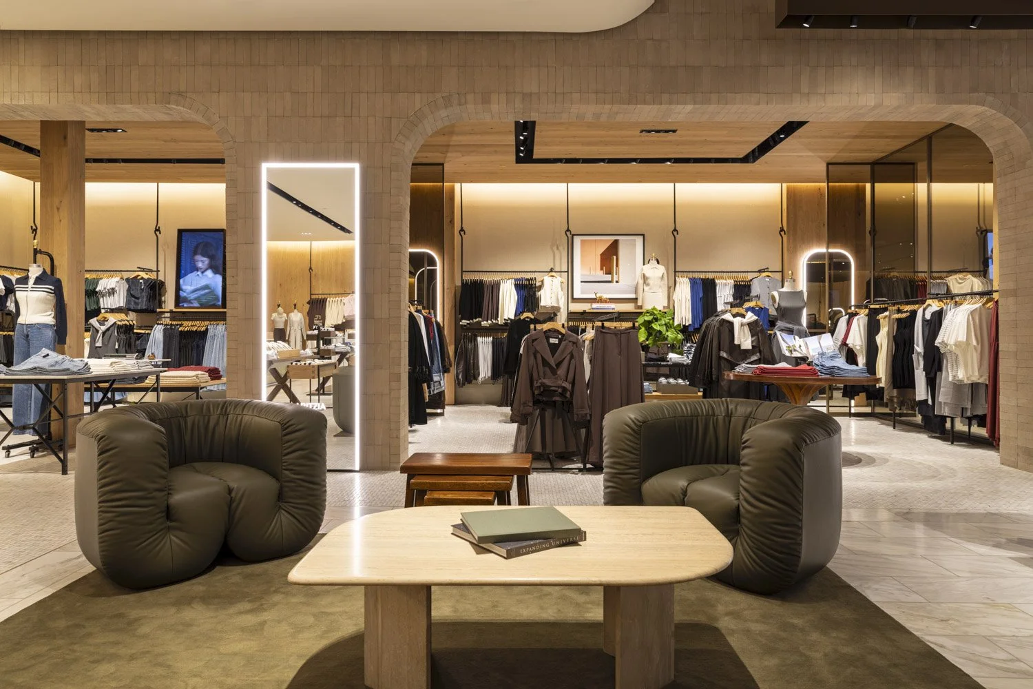 Lounge chairs and a stone coffee table framed by tiled arches and illuminated mirrors at Aritzia, Salt Lake City