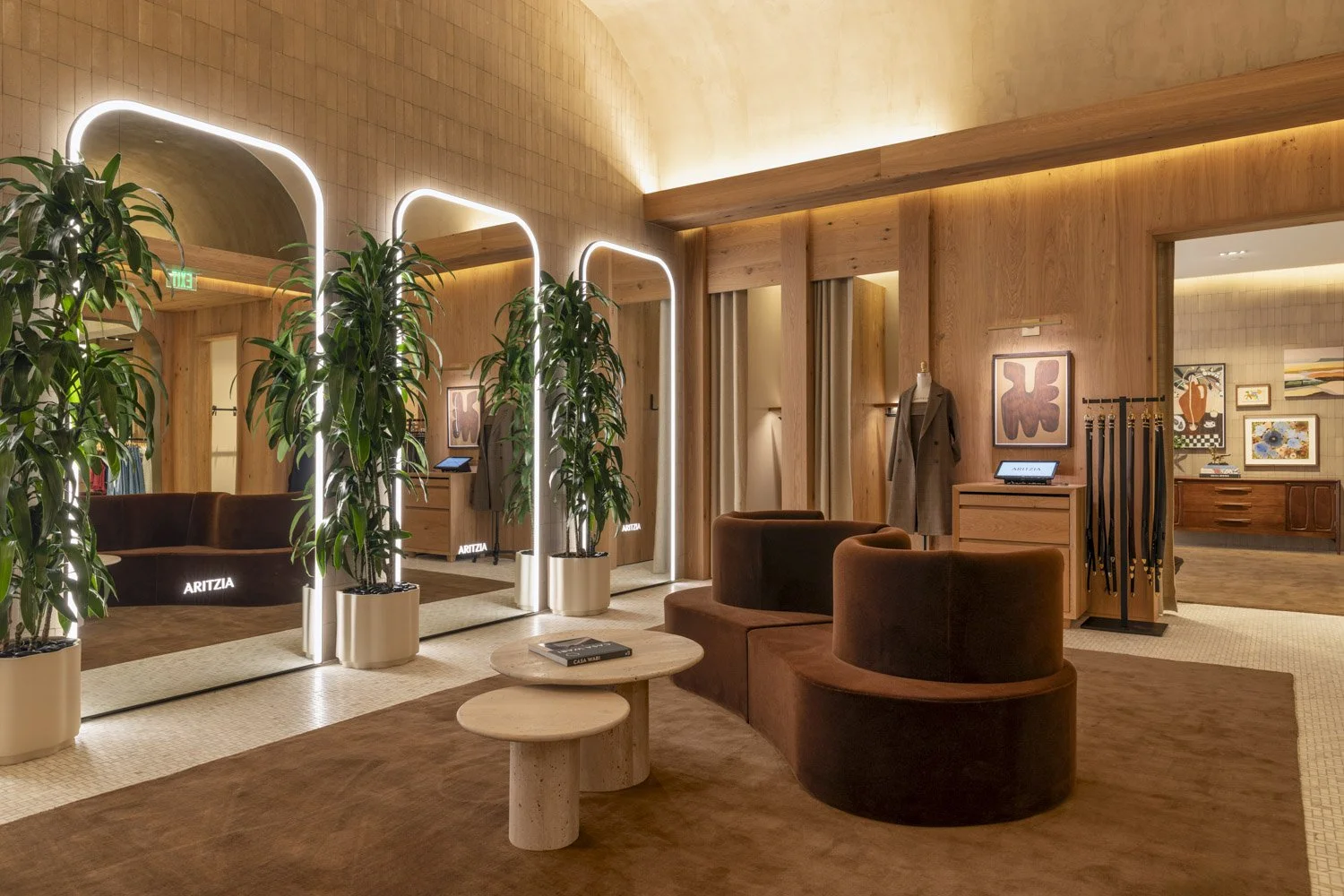 Fitting-room lounge with rounded seating, tall illuminated mirrors, and potted plants at Aritzia, Salt Lake City