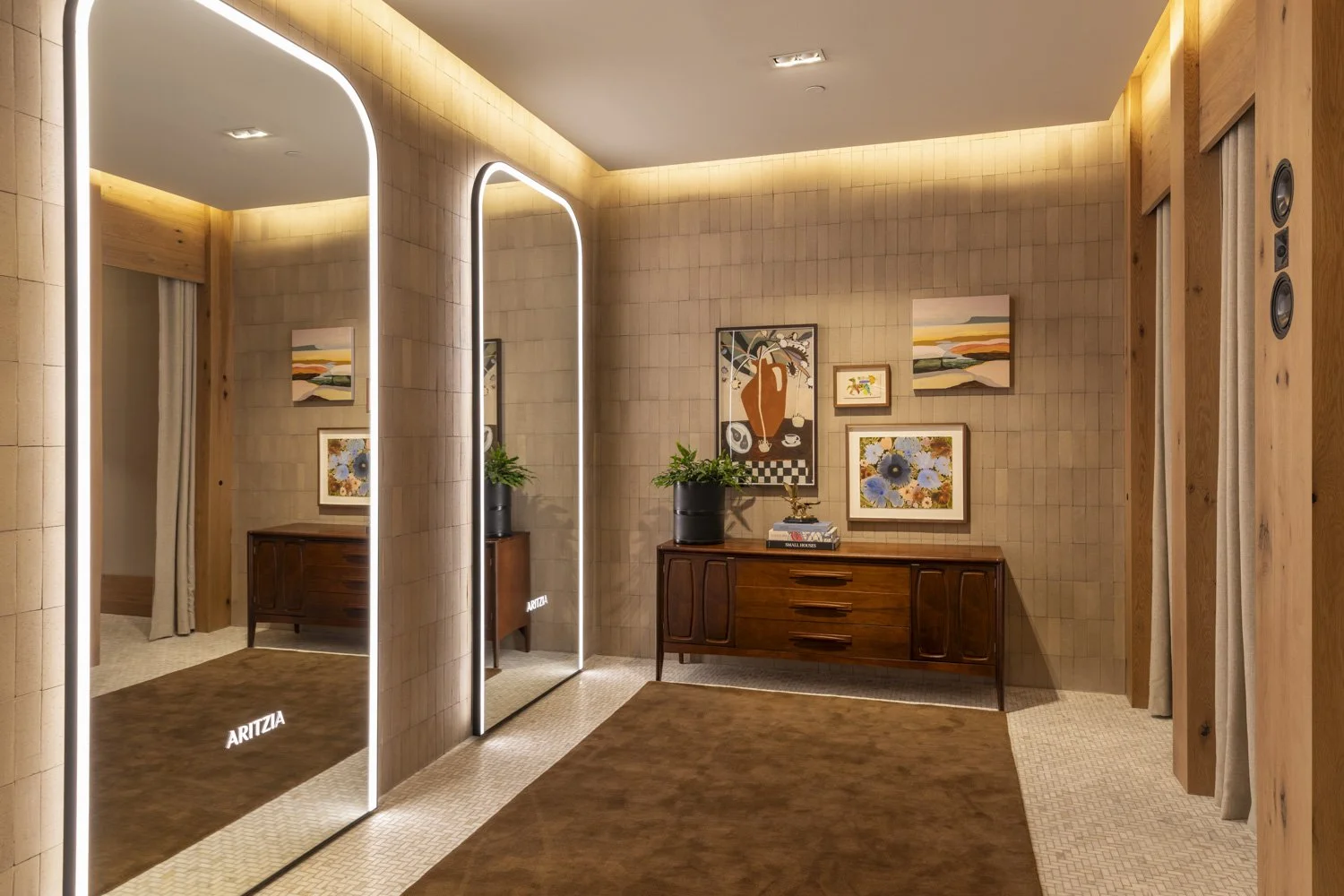 Fitting-room corridor with illuminated mirrors, a timber sideboard, and framed artwork at Aritzia, Salt Lake City